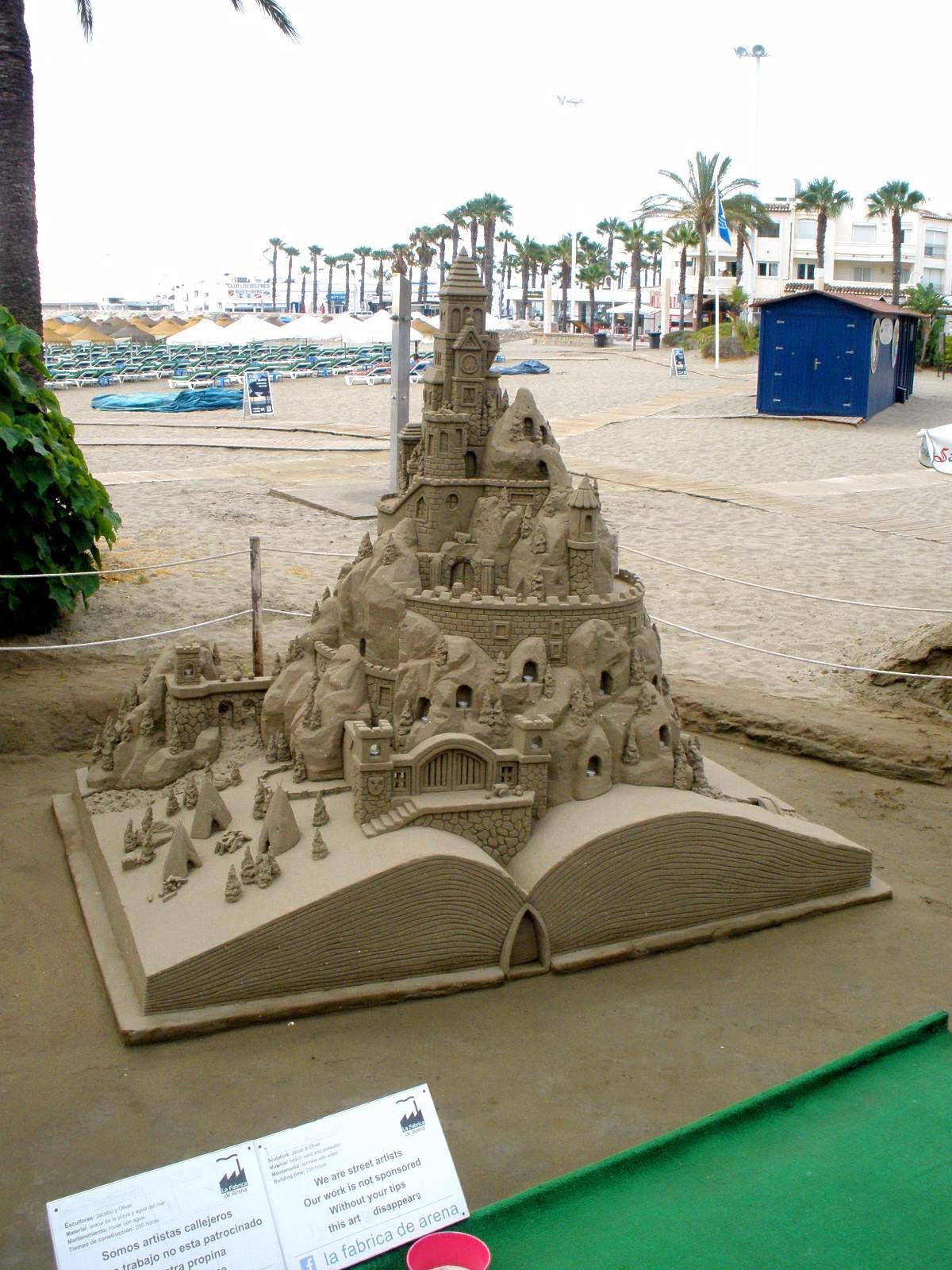 Una detallada y gran escultura de un castillo de arena construida sobre la base de un libro abierto gigante en la arena de la playa.