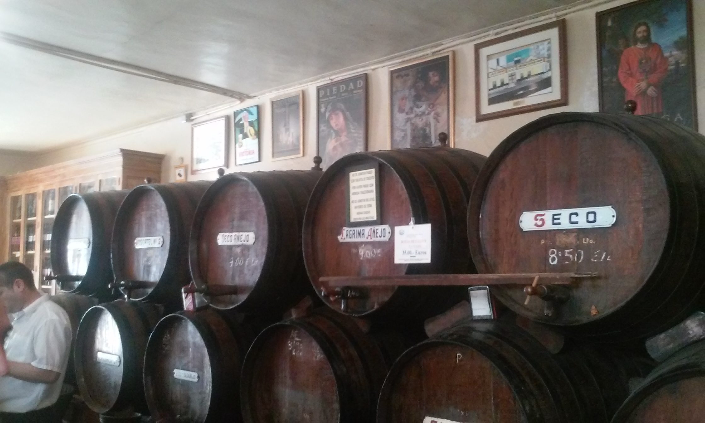 Grandes barriles y toneles de madera alineados en las estanterías de la taberna Antigua Casa de Guardia en Málaga, con etiquetas que indican los nombres de los vinos dulces tradicionales