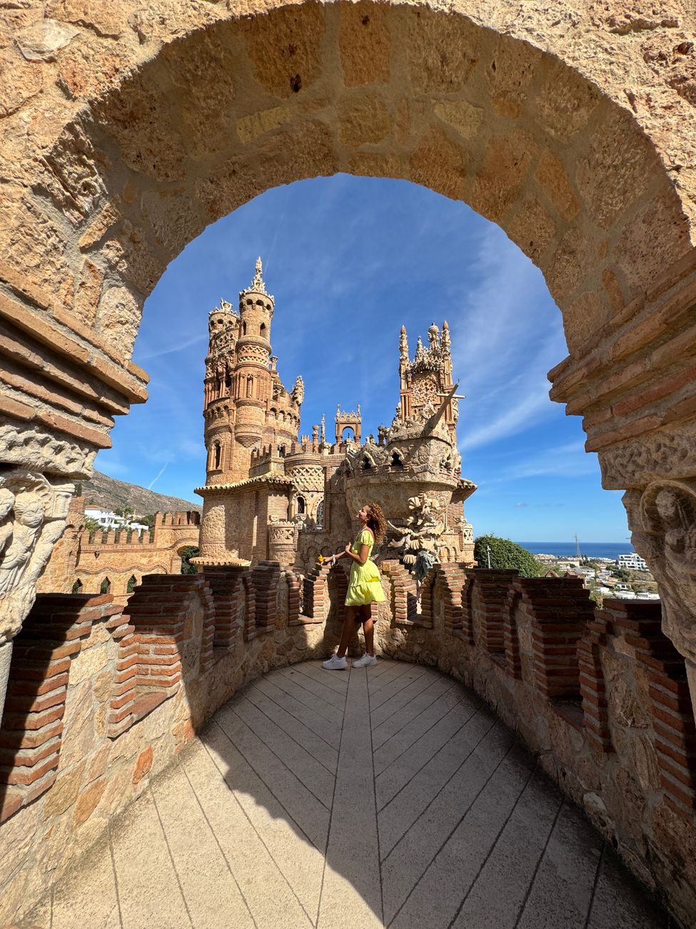 Vista del Castillo de Colomares enmarcado por un arco de piedra con una turista en el centro