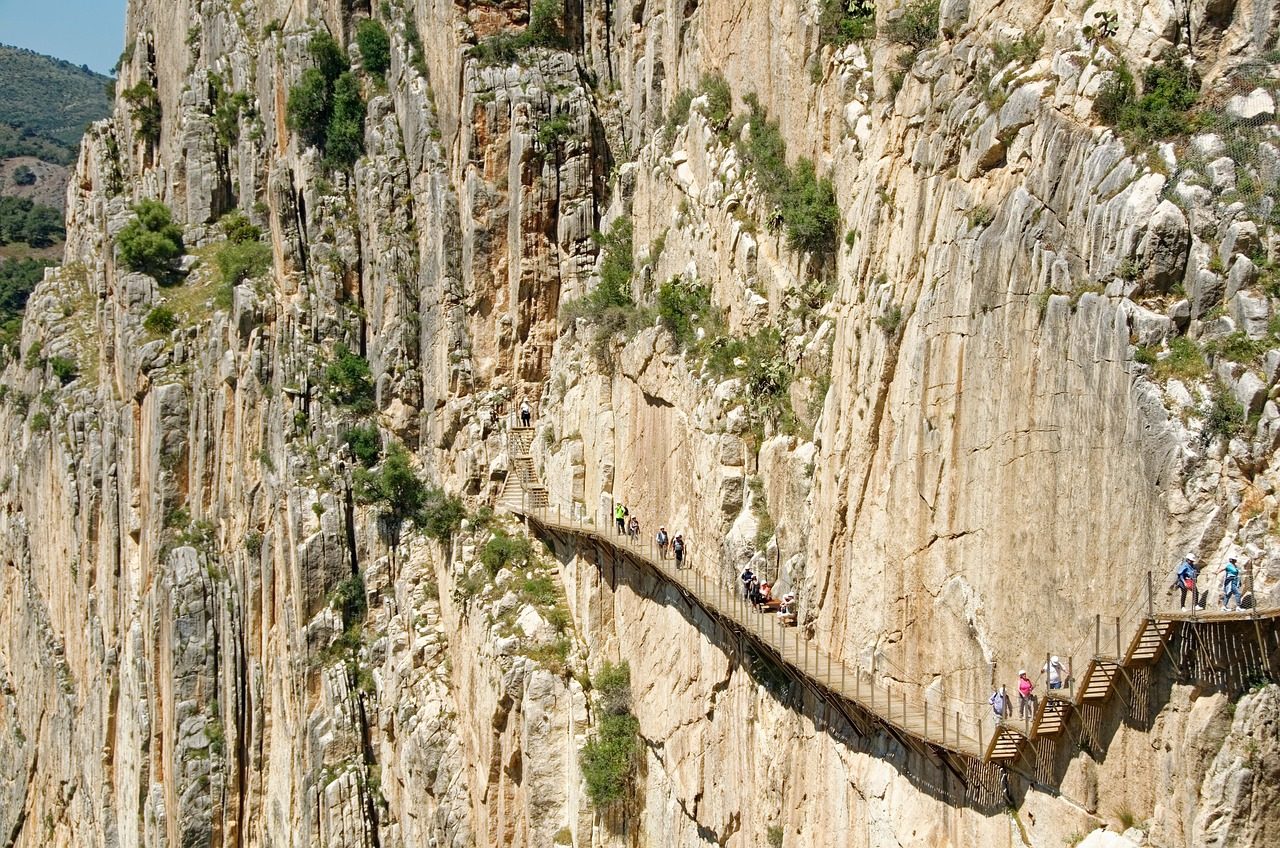 Pasarelas de madera del Caminito del Rey ancladas a una imponente pared de roca vertical con un grupo de senderistas haciendo la ruta guiada en Málaga.
