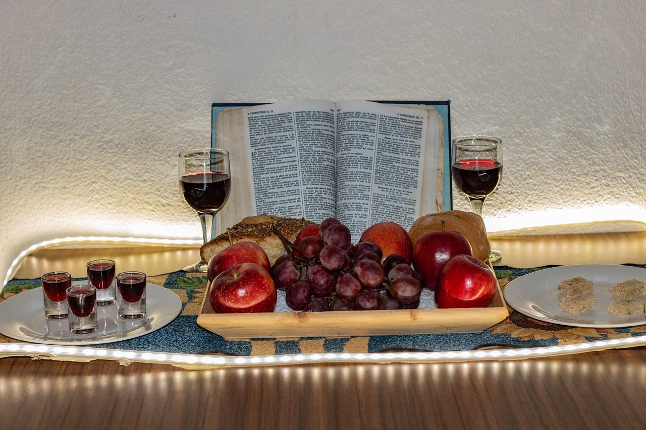 Bodegón con un libro abierto, un racimo de uvas rojas en un cuenco de madera y copas de vino bajo una iluminación cálida
