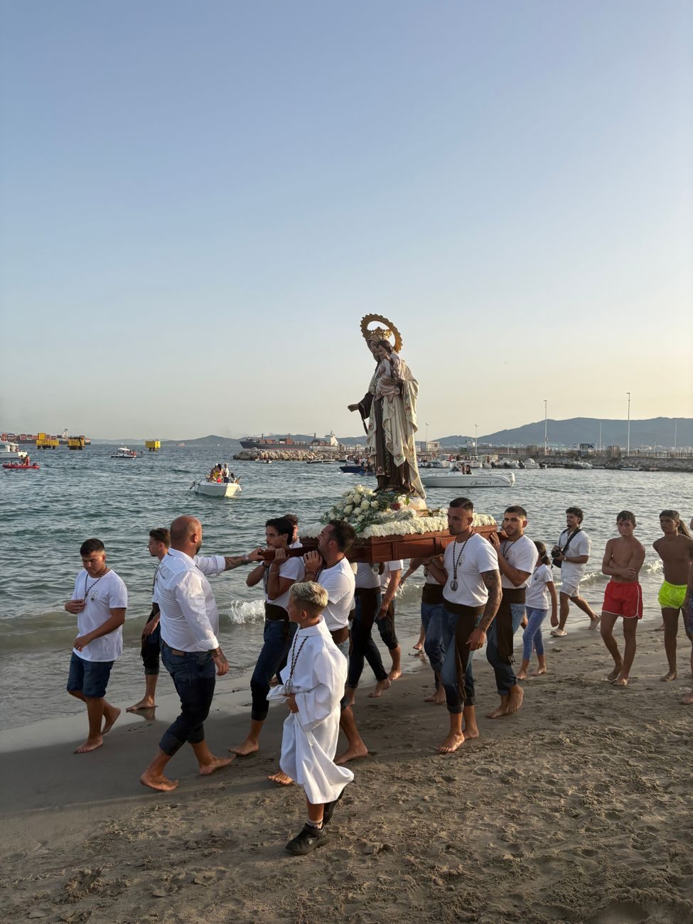 Un grupo de portadores lleva a hombros la estatua de la Virgen del Carmen en la orilla del mar dentro de la playa,