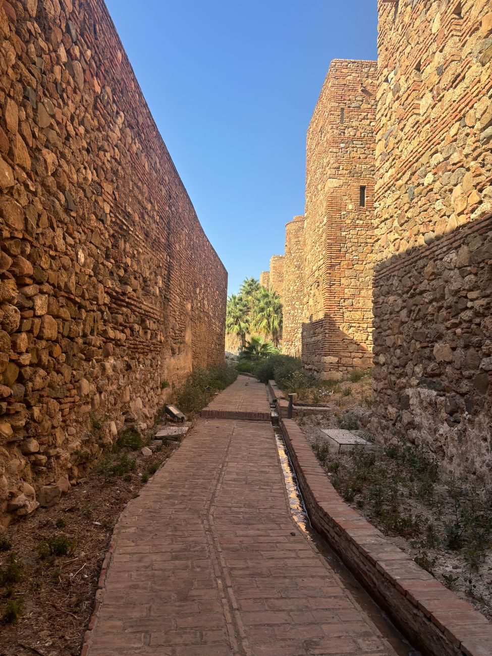 Pasillo empedrado entre las murallas históricas de piedra y ladrillo de la Alcazaba de Málaga.