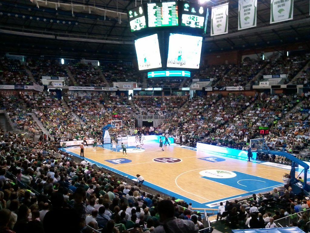 Panoramic view of the Martín Carpena arena filled with fans and the central LED scoreboard turned on during a basketball game.