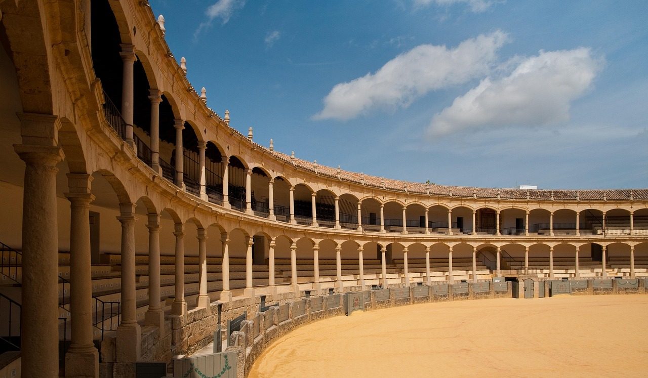 interior de la célebre Plaza de Toros de la Real Maestranza de Caballería de Ronda, destacando su icónica doble galería de arcadas neoclásicas sustentadas por columnas de piedra.