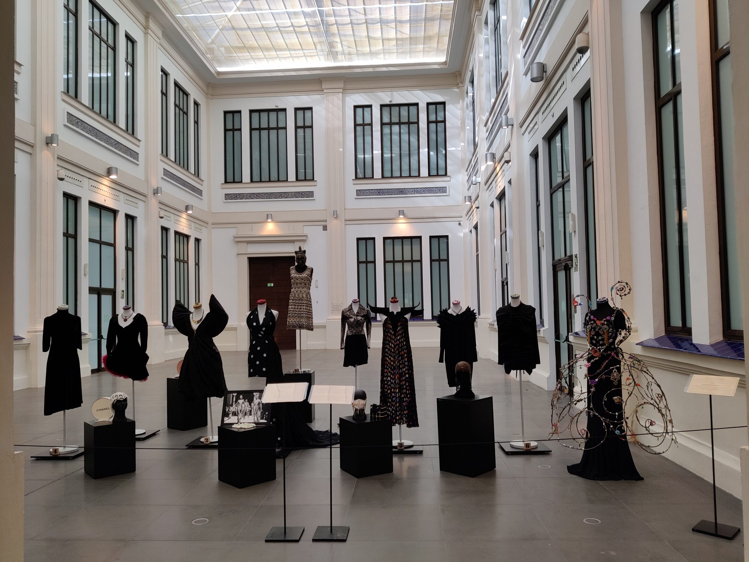 Sala interior de desfiles y colecciones: El gran patio central interior con luz natural donde se disponen los vestidos de diseñadores legendarios (como Chanel, Dior o Balenciaga) junto a los vehículos