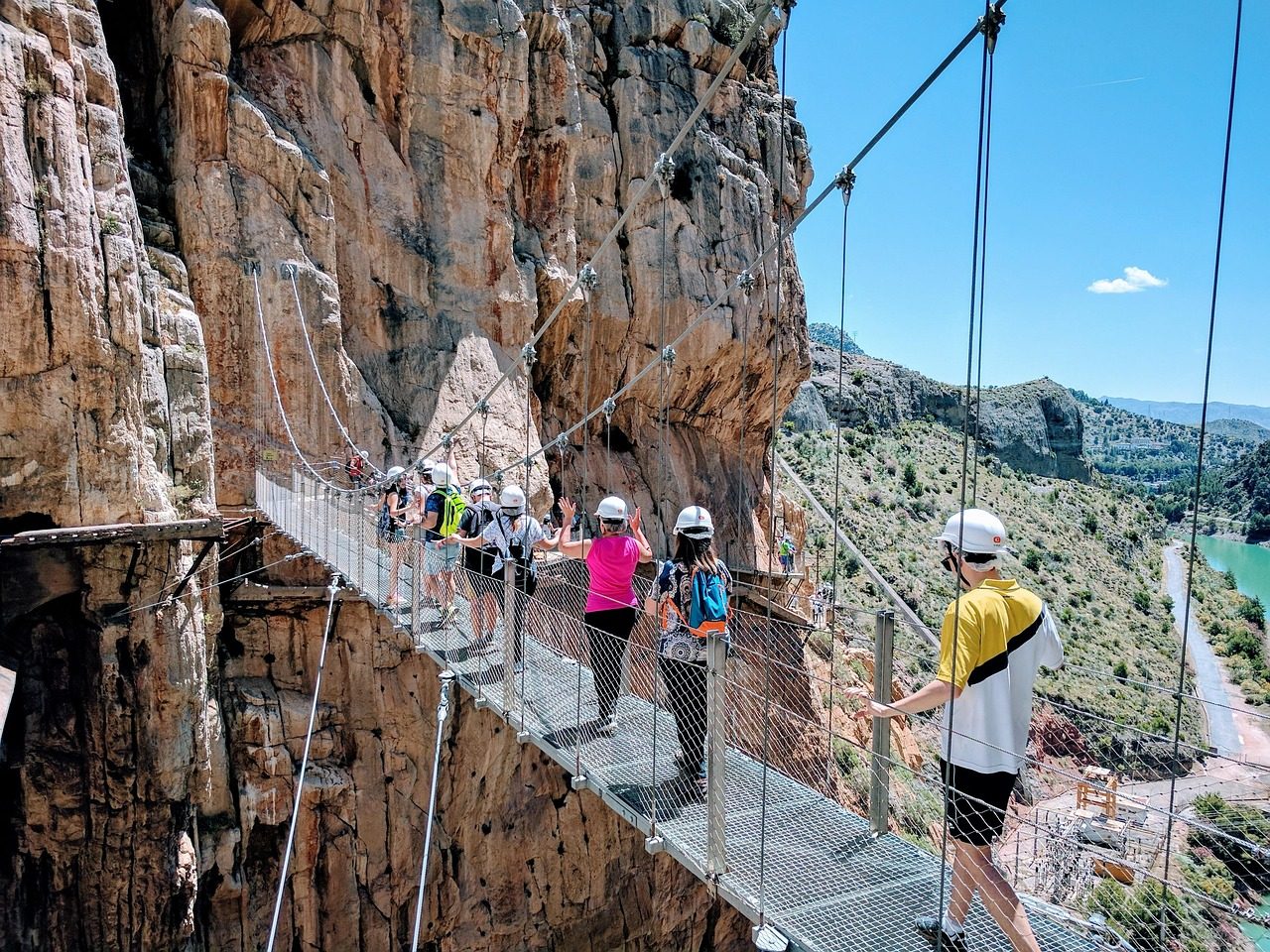Excursionistas con casco cruzando el puente colgante del Caminito del Rey en el Desfiladero de los Gaitanes, Málaga.