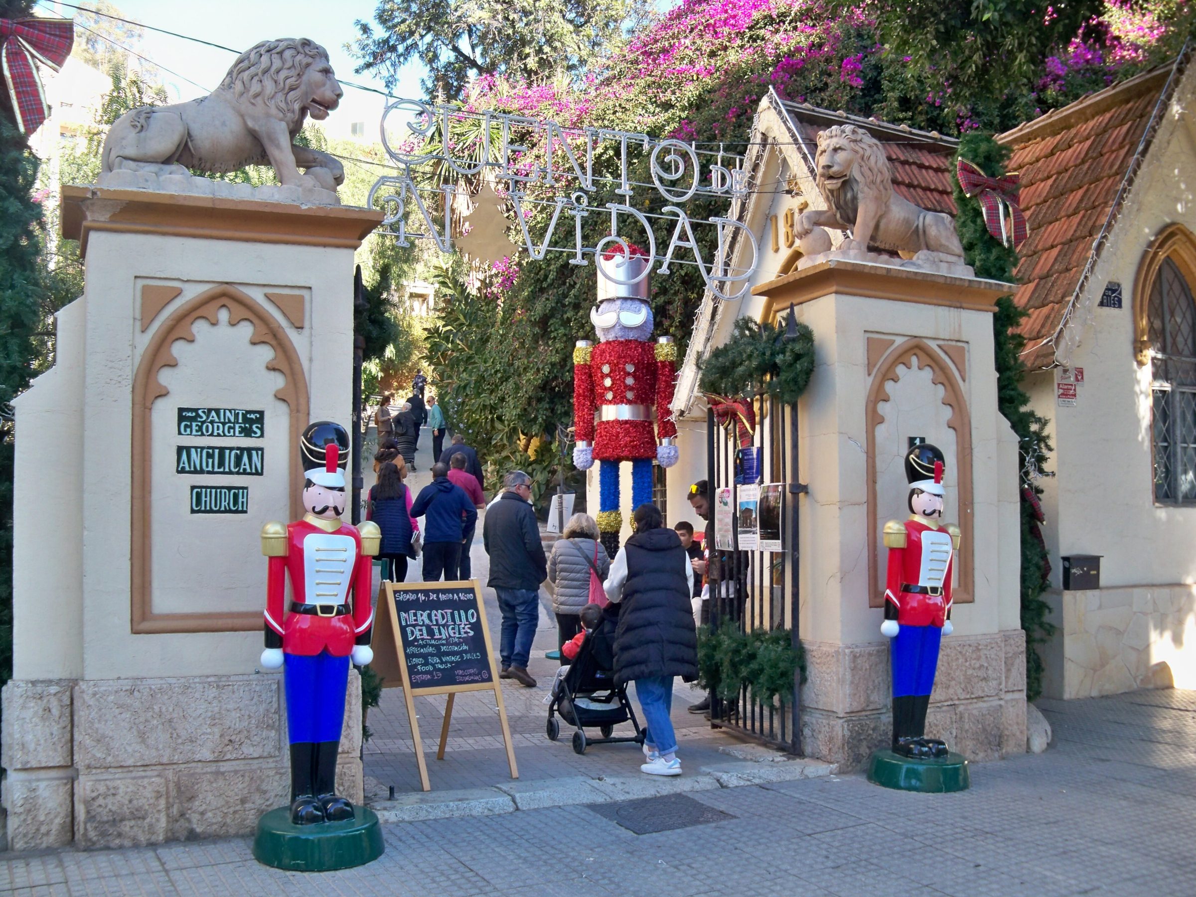 Entrada neogótica del Cementerio Inglés de Málaga con leones de piedra esculpidos en las columnas y decorada con figuras de soldados cascanueces gigantes y un gran Papá Noel durante el mercado navideño