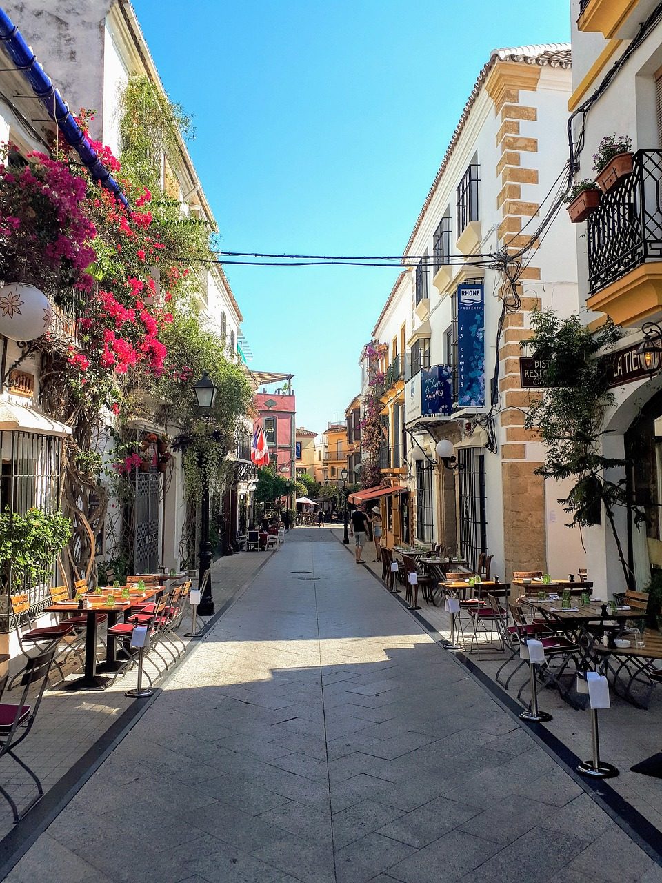 Calle Pantaleón en el Casco Antiguo de Marbella, una vía peatonal estrecha con terrazas de restaurantes, fachadas tradicionales y llamativas buganvillas fucsias en flor bajo un cielo despejado