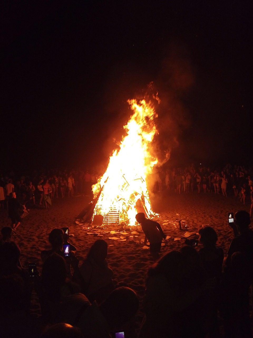 Una gran hoguera arde con intensas llamas naranjas en la arena de la playa durante la noche,