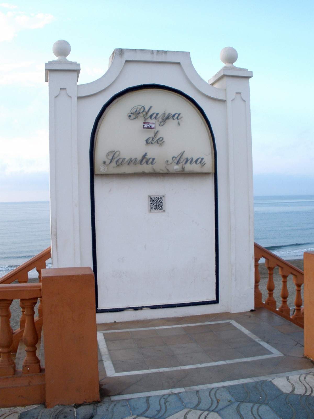 Cartel de obra blanco con letras oscuras donde se lee "Playa de Santa Ana", situado en el acceso al paseo marítimo de Benalmádena.