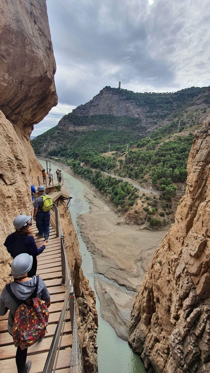 Turistas con cascos de protección recorriendo las pasarelas de madera ancladas a las verticales paredes de roca caliza en el Caminito del Rey.