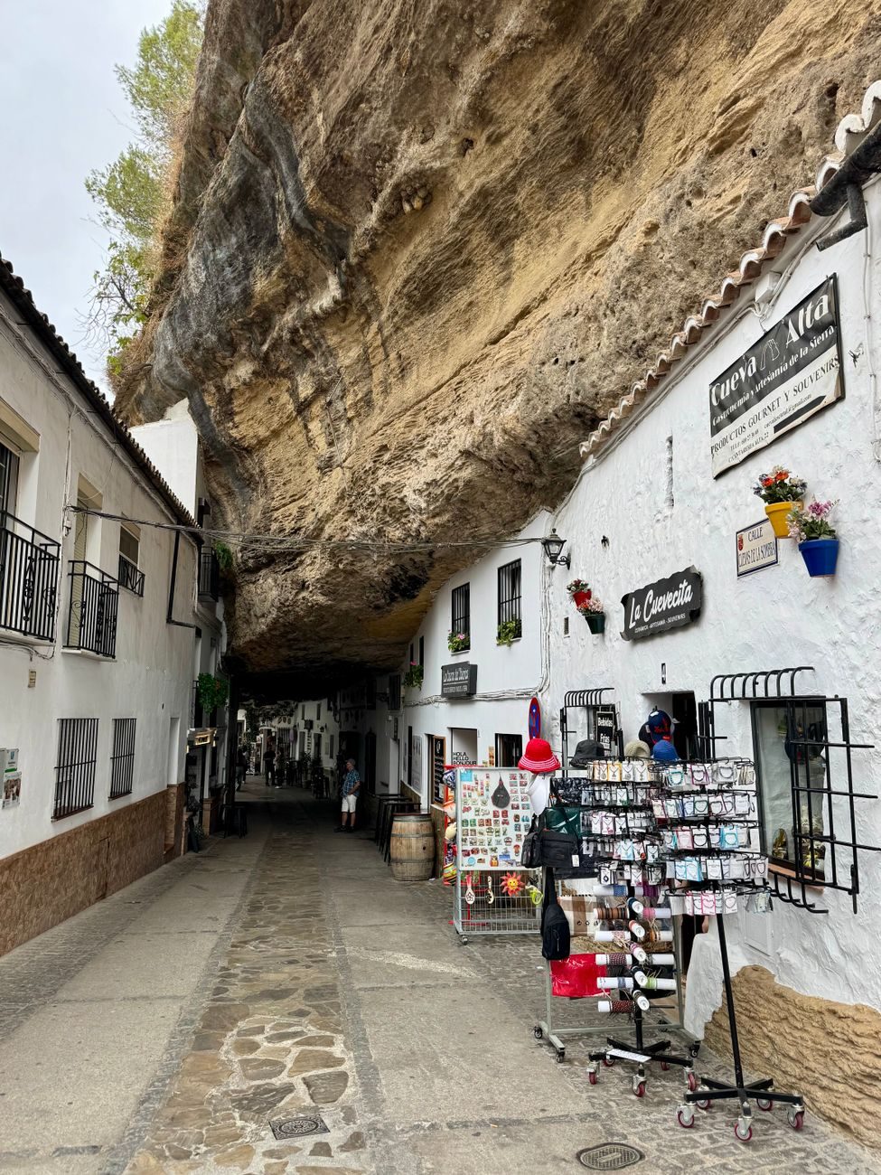Calle estrecha y empedrada en Setenil de las Bodegas con casas tradicionales de fachadas blancas construidas directamente bajo una enorme roca suspendida de la montaña.